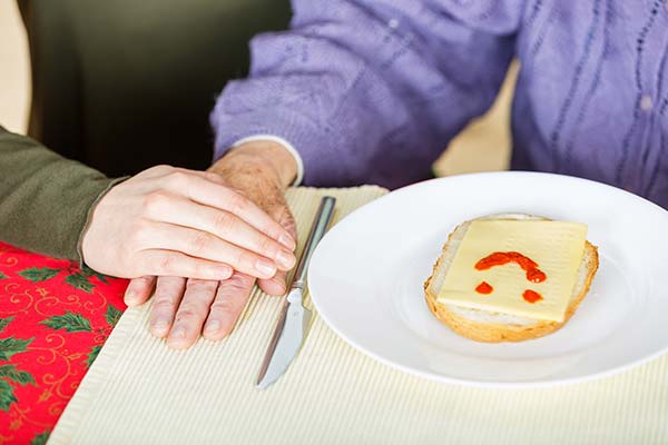 Caregiver with hand over hand of senior client with smiley face on open-face sandwich