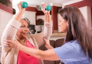 Caregiver helping senior woman with weight lifting program